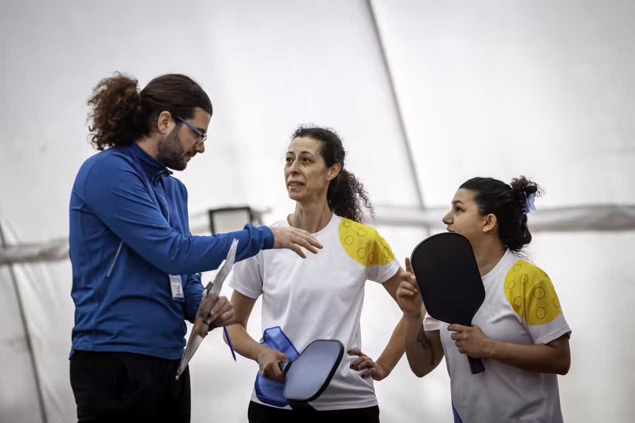 A male teaching two females to play pickleball